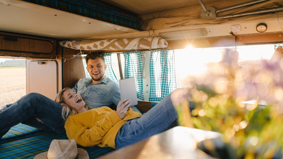 Happy young couple looking at tablet inside camper van